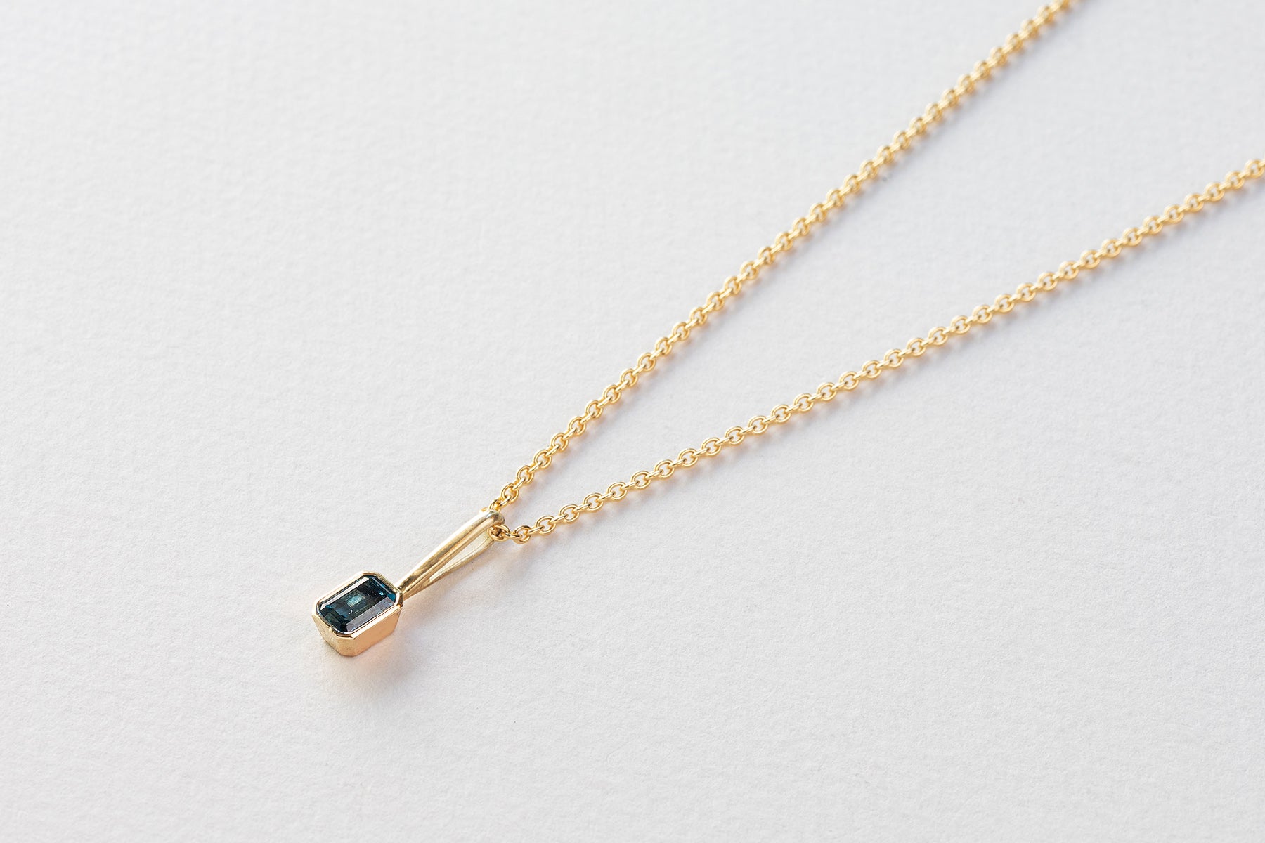 שרשרת חוליות זהב עדינות ותליון זהב עם וו ארוך בצורת מלבן משובץ טורמלין כחול.