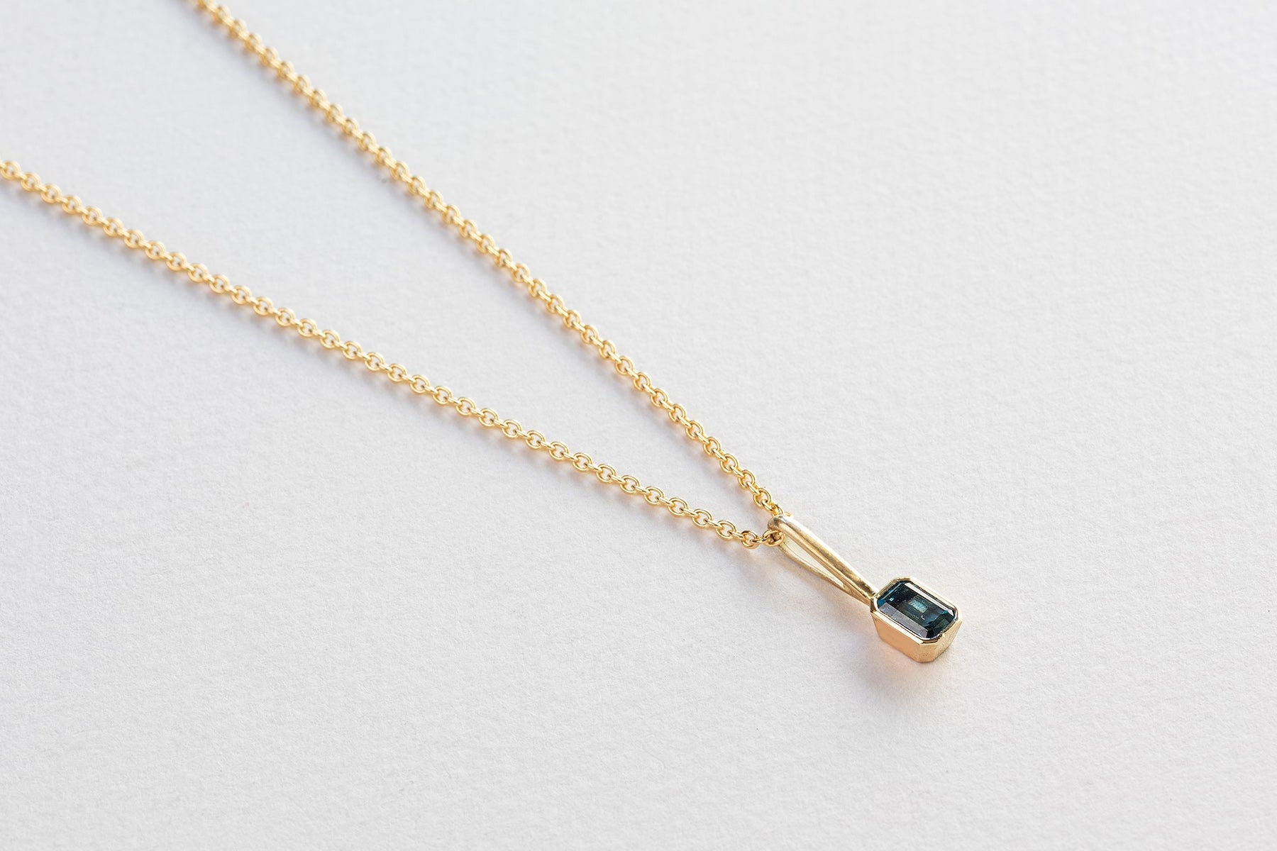 שרשרת חוליות זהב עדינות ותליון זהב עם וו ארוך בצורת מלבן משובץ טורמלין כחול.