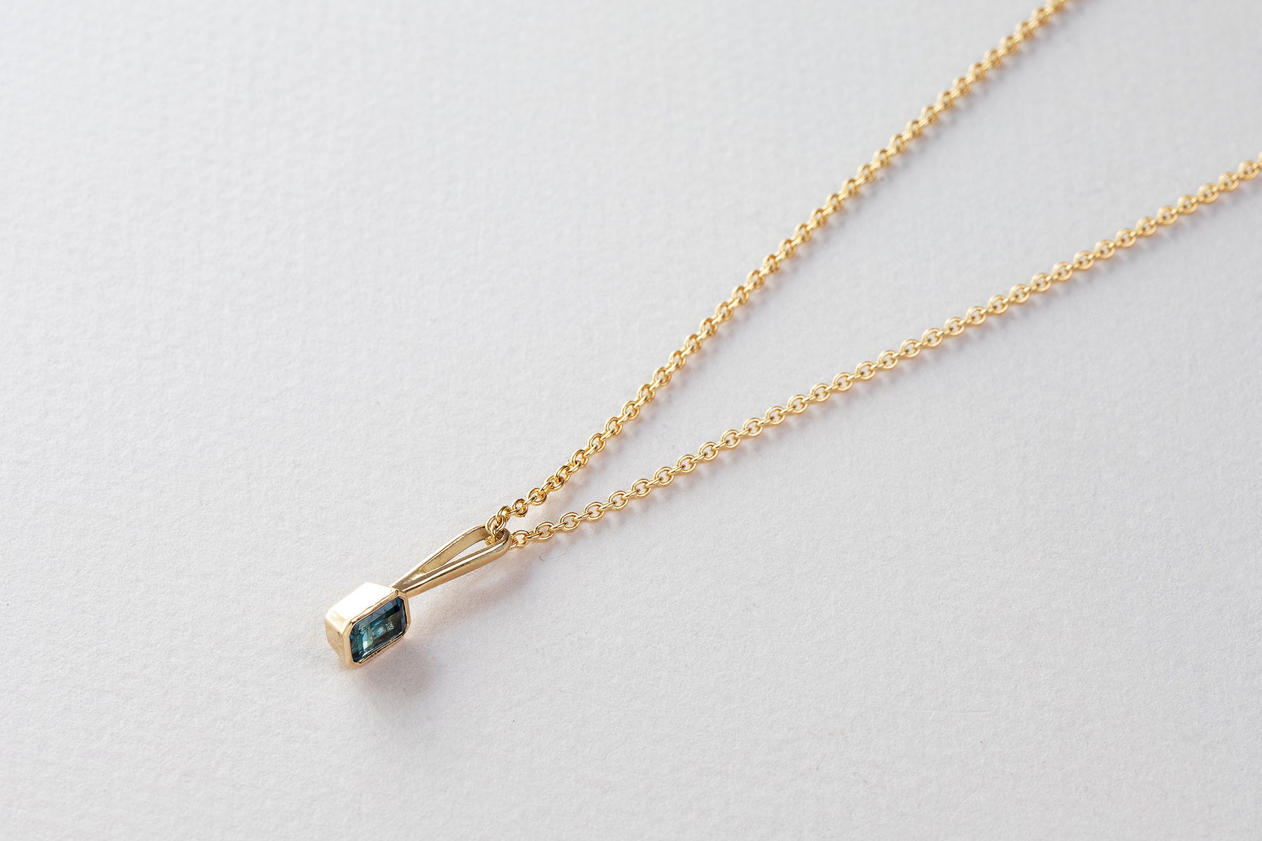 שרשרת חוליות זהב עדינות ותליון זהב עם וו ארוך בצורת מלבן משובץ טורמלין כחול.