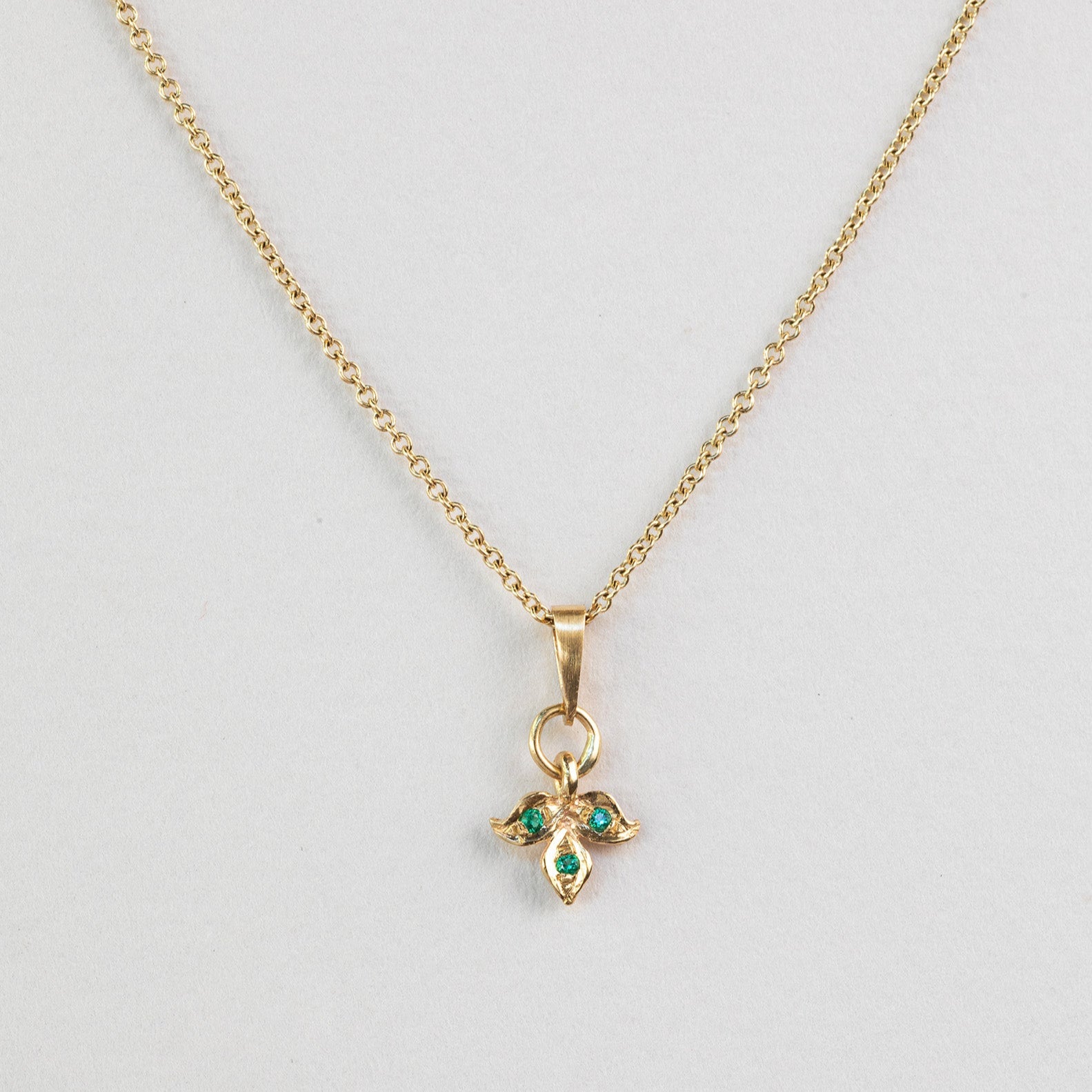 שרשרת זהב עדינה עם תליון עלה זהב משובץ בשלושה אבני אמרלד ירוקות.