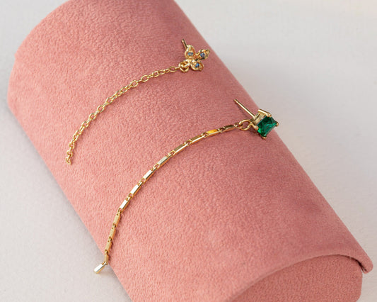 עגיל זהב מעוצב צמוד לאוזן עם אמרלד מעבדה מעויין שממנו יוצאת שרשרת זהב  ועגיל תלתן זהב משובץ בלו טופז עם שרשת חוליות זהב