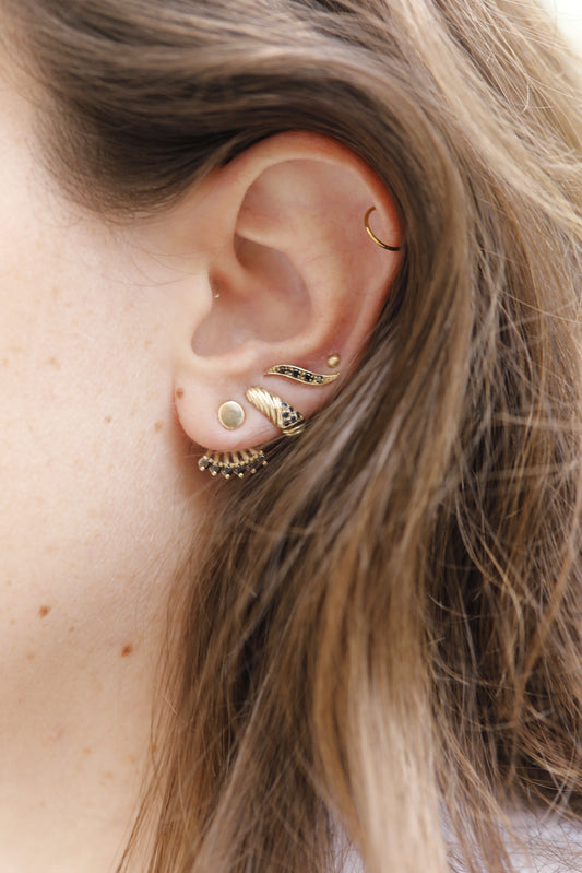 תקריב של אוזן מעוטרת עגילי זהב, כולל עגיל זהב וינטאג׳- מורן - ספיר המהמם מ-Hydra Jewelry Studio. העגילים כוללים חישוקים קטנים, ניטים מורכבים ועיצוב בצורת בורג. שיער חום בהיר מכסה חלקית את האוזן, ומשפר את המראה האלגנטי.