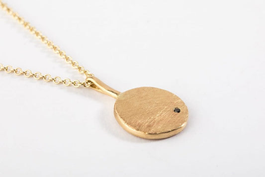 שרשרת זהב עם תליון בצורת מטבע זהב שעליו משובצת אבן יהלום שחור עדינה. המטבע מחובר עם וו זהב. 