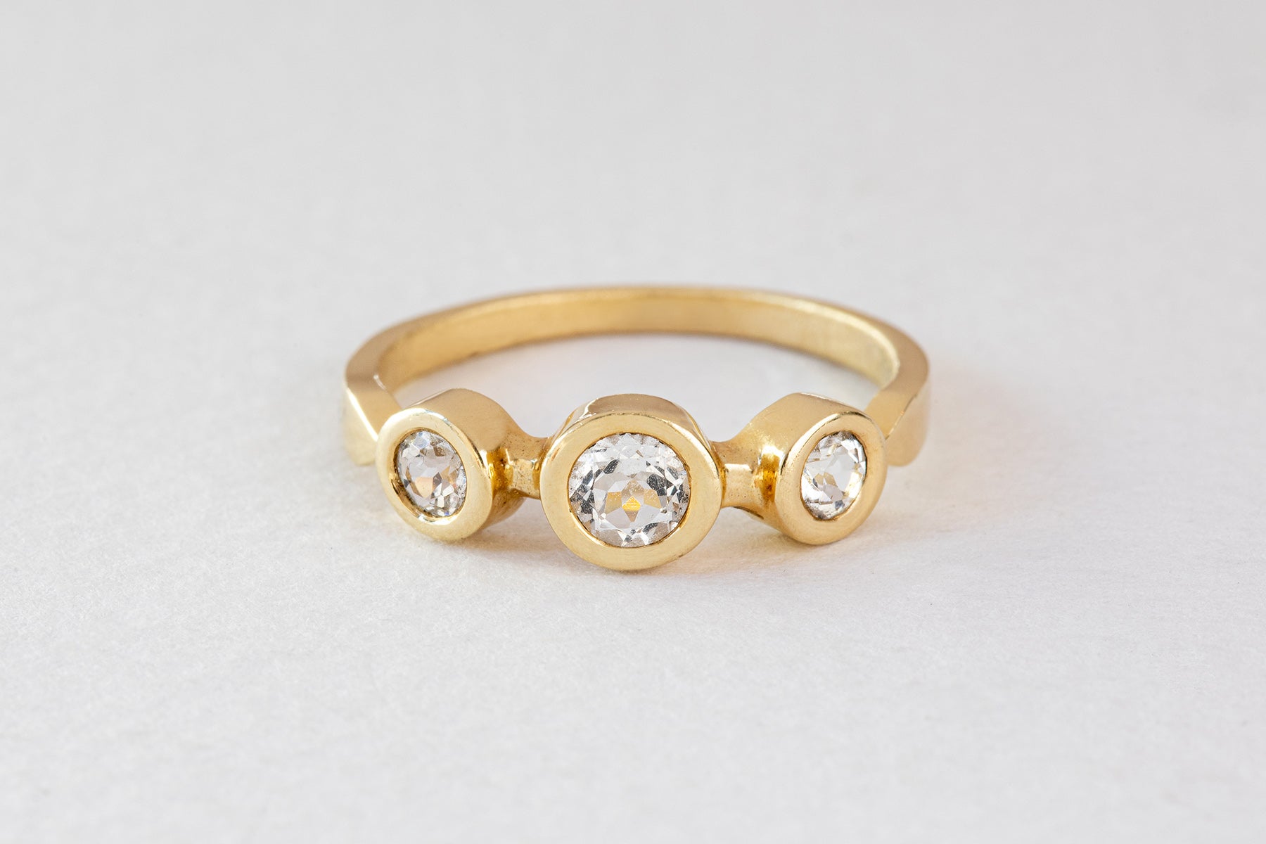 טבעת זהב מסטודיו Hydra Jewelry, טבעת זהב אביב - טופז לבן, מציגה שלוש אבני טופז לבנות עגולות בעיצוב אלגנטי ומודרני על רקע אפור בהיר.