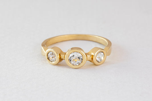 טבעת זהב מסטודיו Hydra Jewelry, טבעת זהב אביב - טופז לבן, מציגה שלוש אבני טופז לבנות עגולות בעיצוב אלגנטי ומודרני על רקע אפור בהיר.