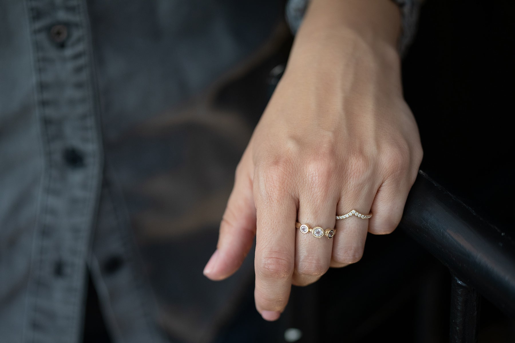 יד נוגעת קלות במעקה כהה, עונדת טבעת מותאמת אישית ו"טבעת זהב אביב - טופז לבן" מבית Hydra Jewelry Studio. האדם לבוש בחולצה מכופתרת כהה.
